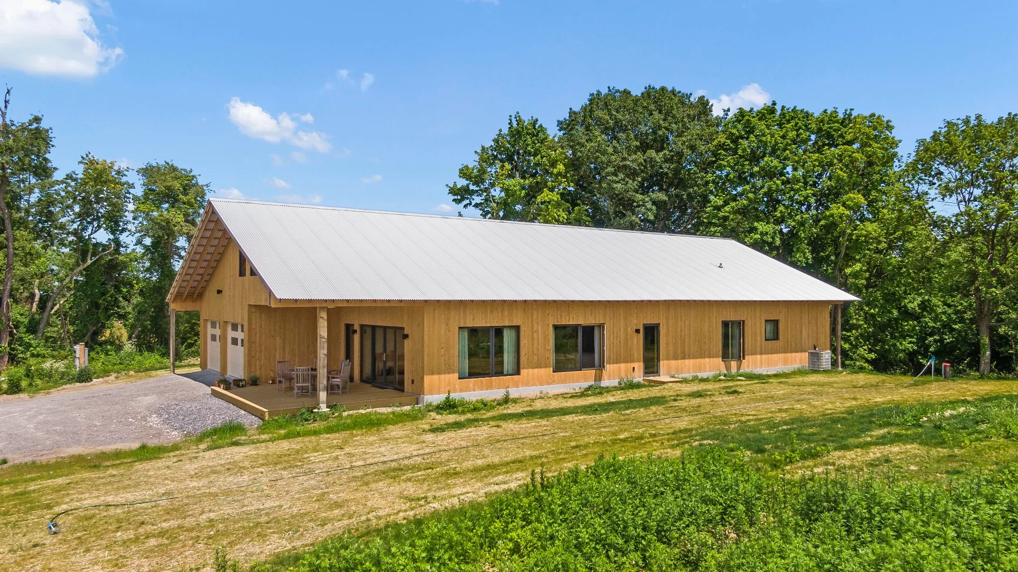 Aerial view of a modern timber-clad home with metal roof surrounded by trees and open land